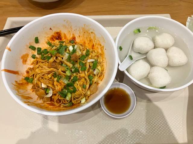 メニュー、Fishball Noodles Dryの実際の写真。辛そうな見た目のドライヌードルとフィッシュボールが浮いたスープのセット。