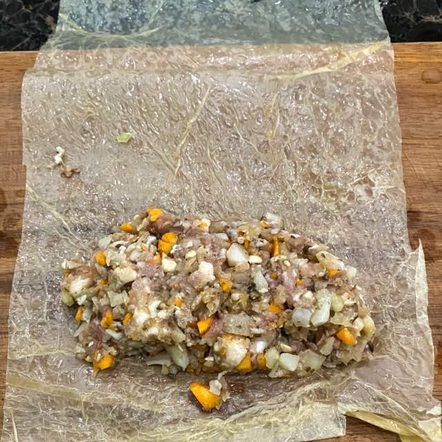 刻んだ具を混ぜ合わせて寝かせた後、揚げ湯葉の皮で包むときの様子。長方形の湯葉の手前に具をのせ、左右を巻き込んで丸めていく。